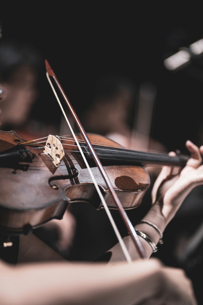 A woman plays a violin in a classical symphony.